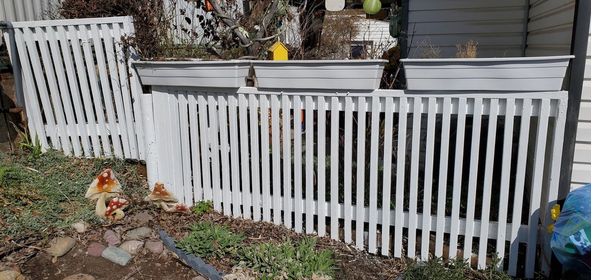 After: Grey, peeling pickets and red-brown posts, with the planter boxes above, all painted white.