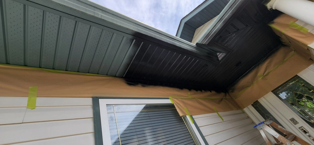 Soffit mid-job: masking paper and tape protect the siding and window below.
